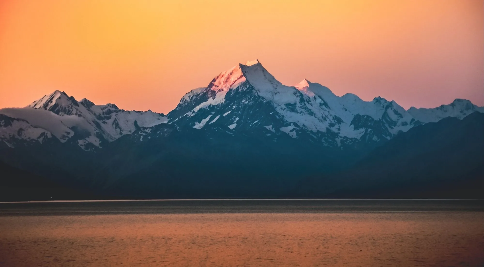 Aoraki/Mount Cook catching pink light at sunset above a dark ridge