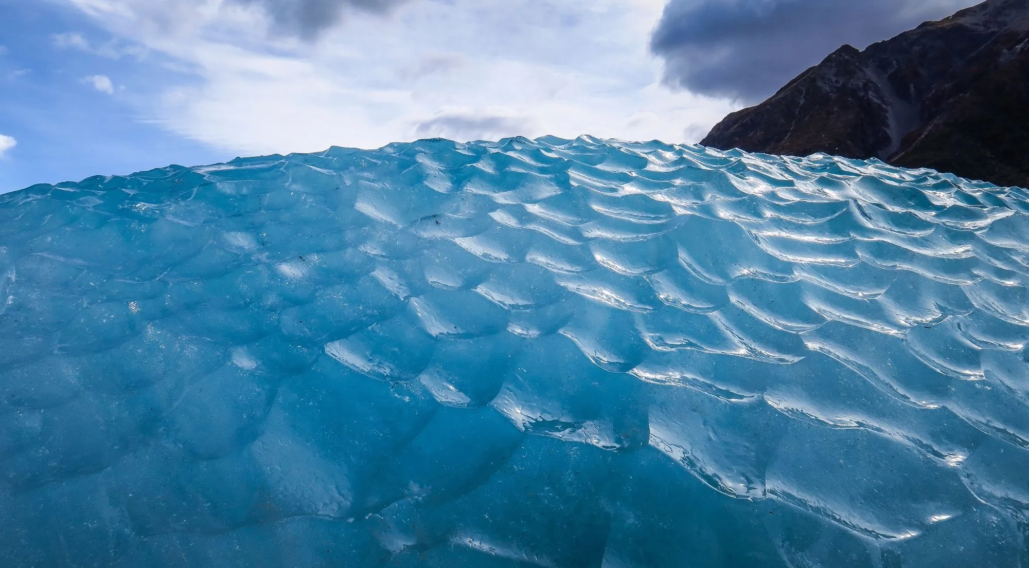 Close-up of sculpted blue glacier ice under a cloudy sky