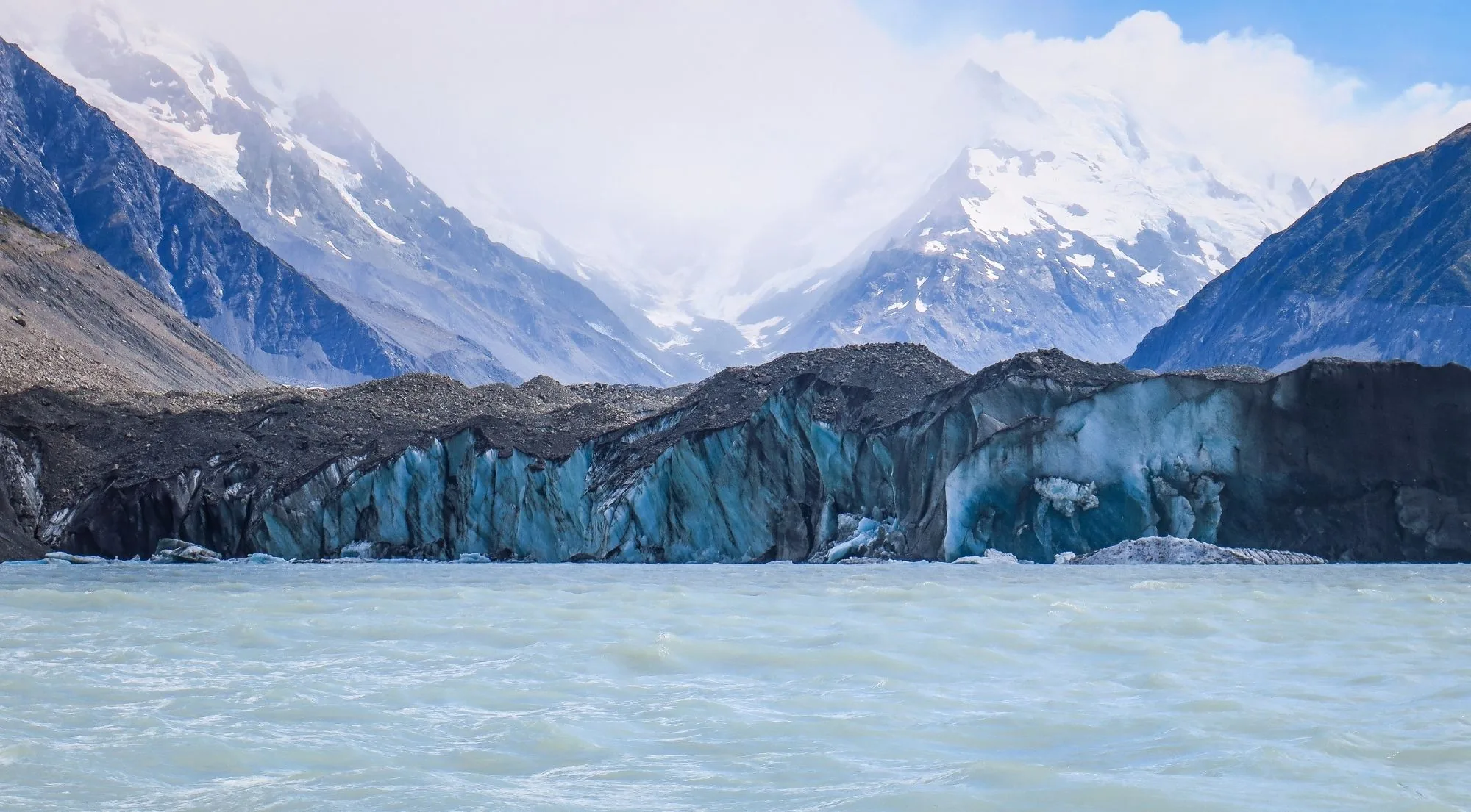 Glacier ice face on a glacial lake with snow-covered peaks behind