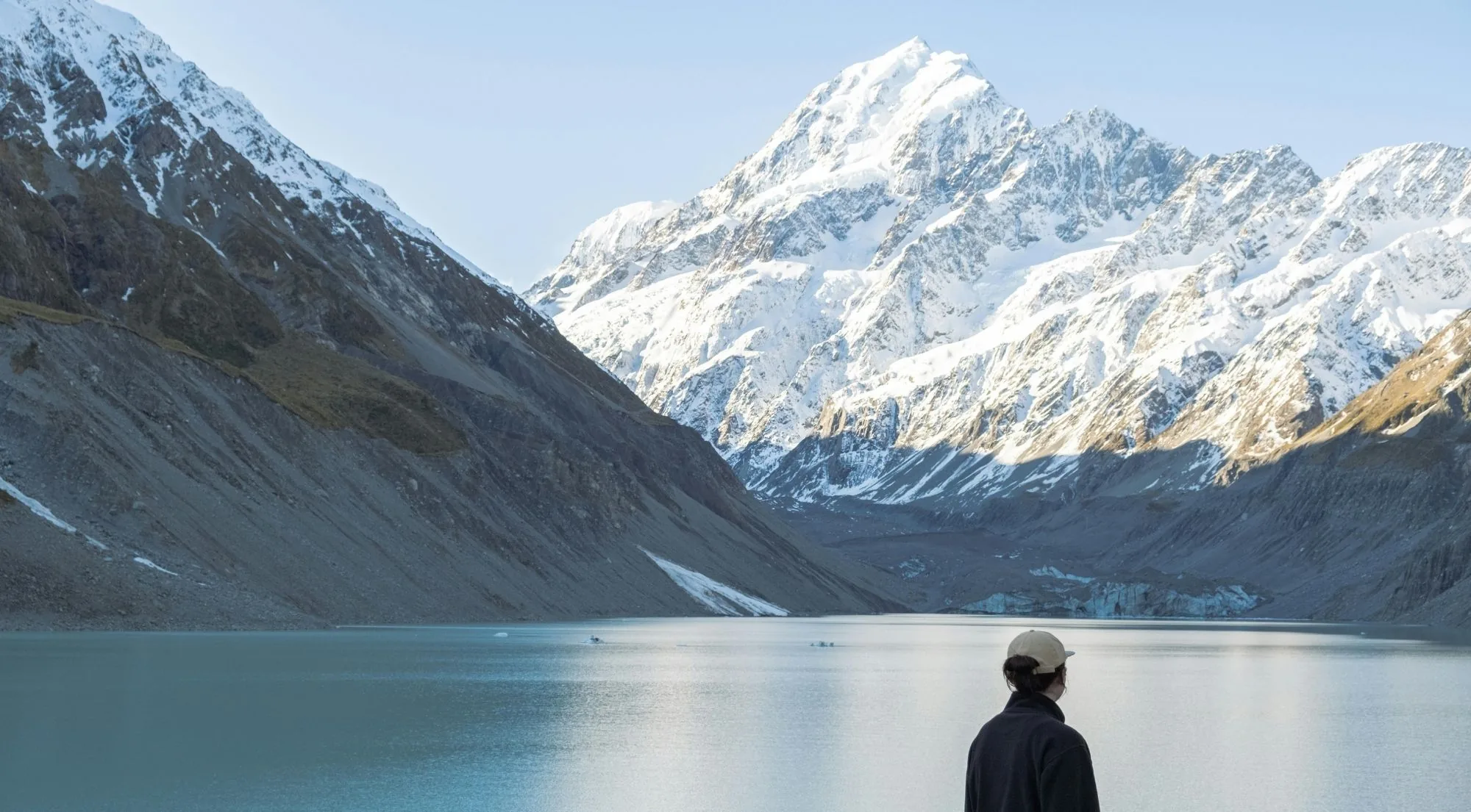A walker looking across a glacier lake toward Aoraki/Mount Cook
