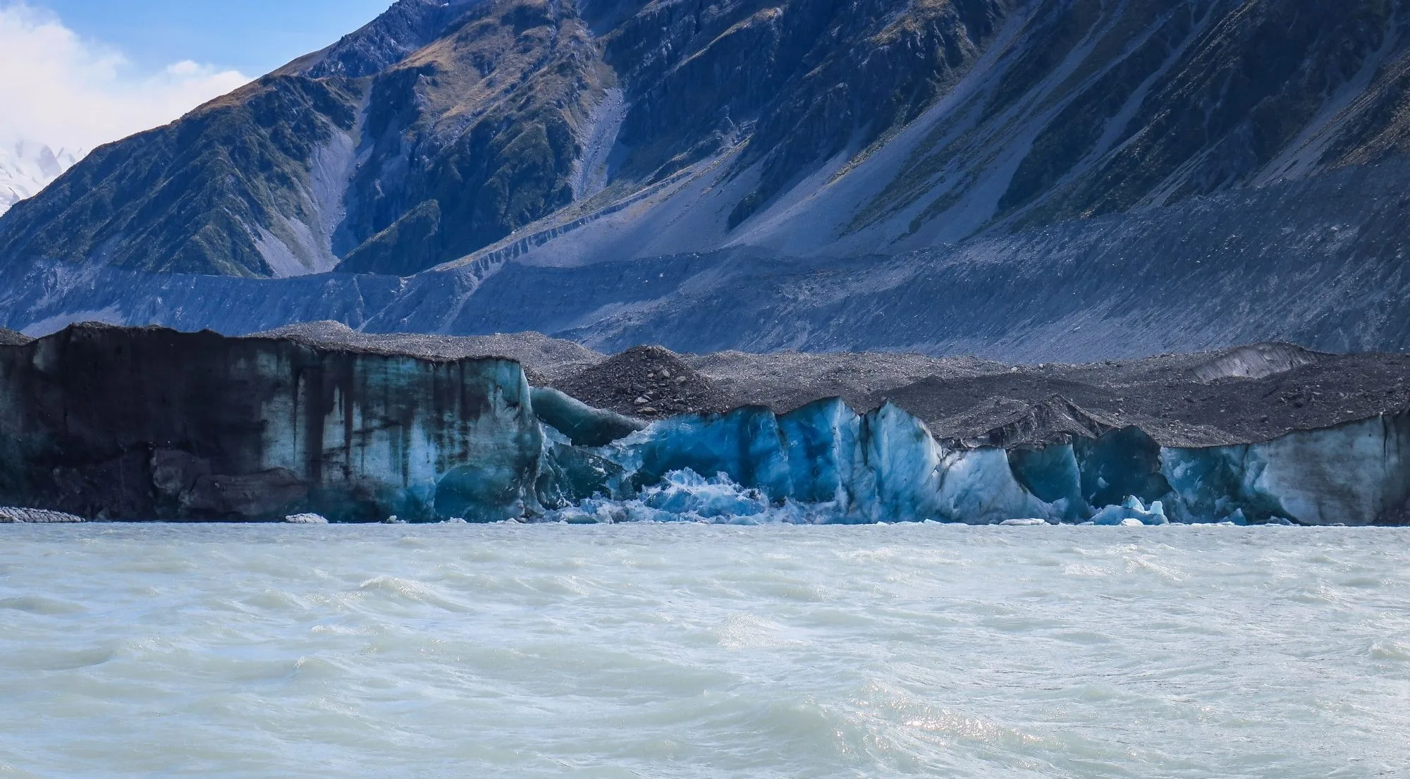 Grey and blue ice face of a glacier terminal meeting a milky meltwater lake