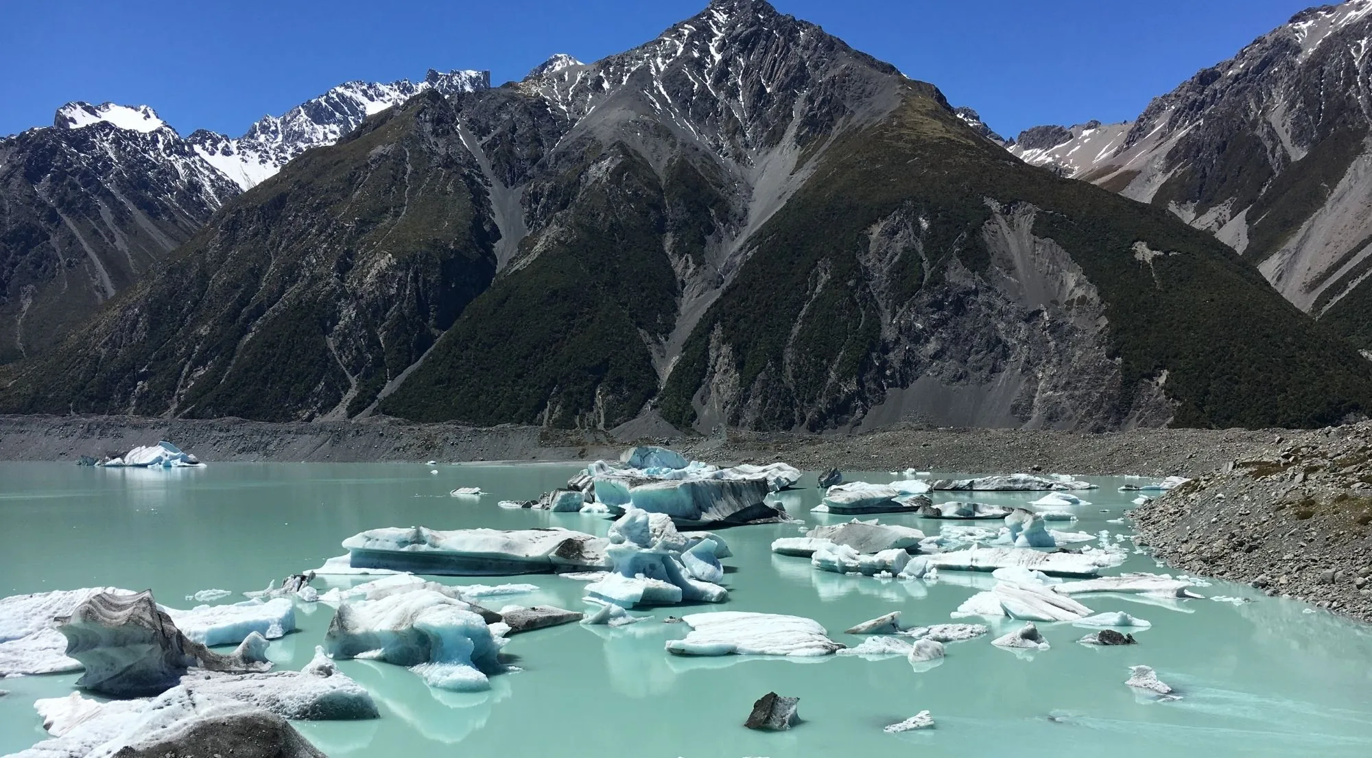 Icebergs floating on Tasman Lake below dark mountain slopes