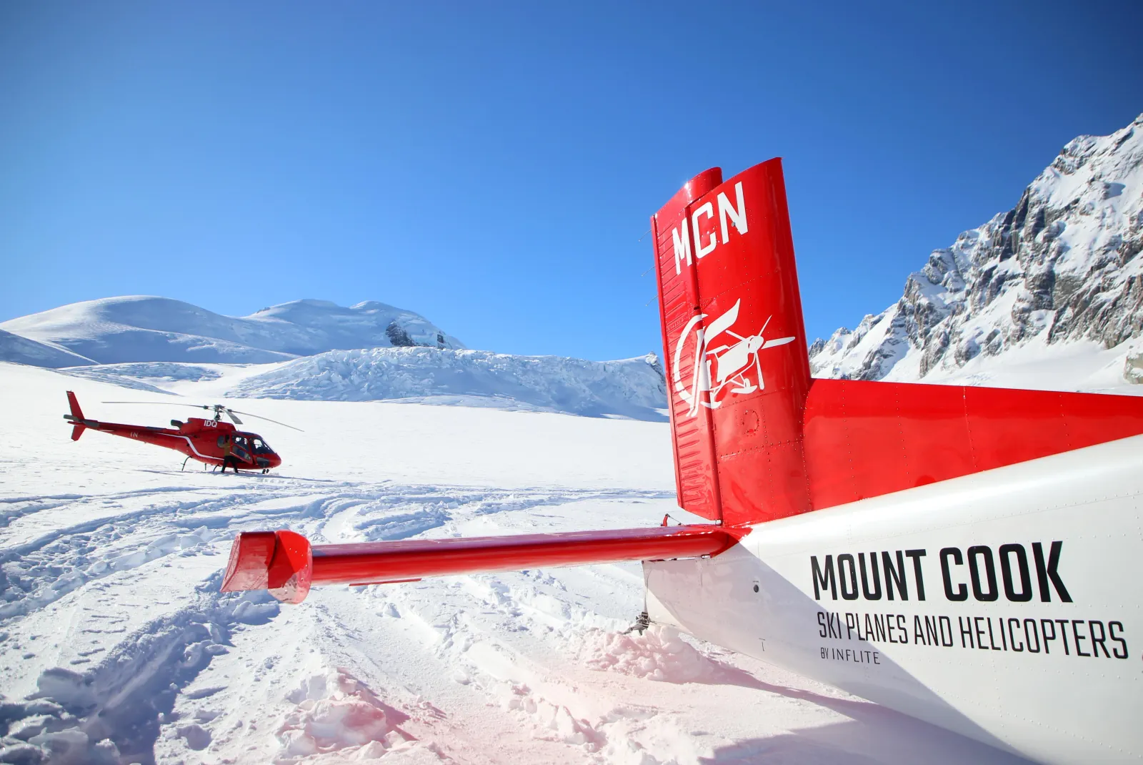 Red tail of a Mount Cook Ski Planes aircraft on the glacier, with a red helicopter behind