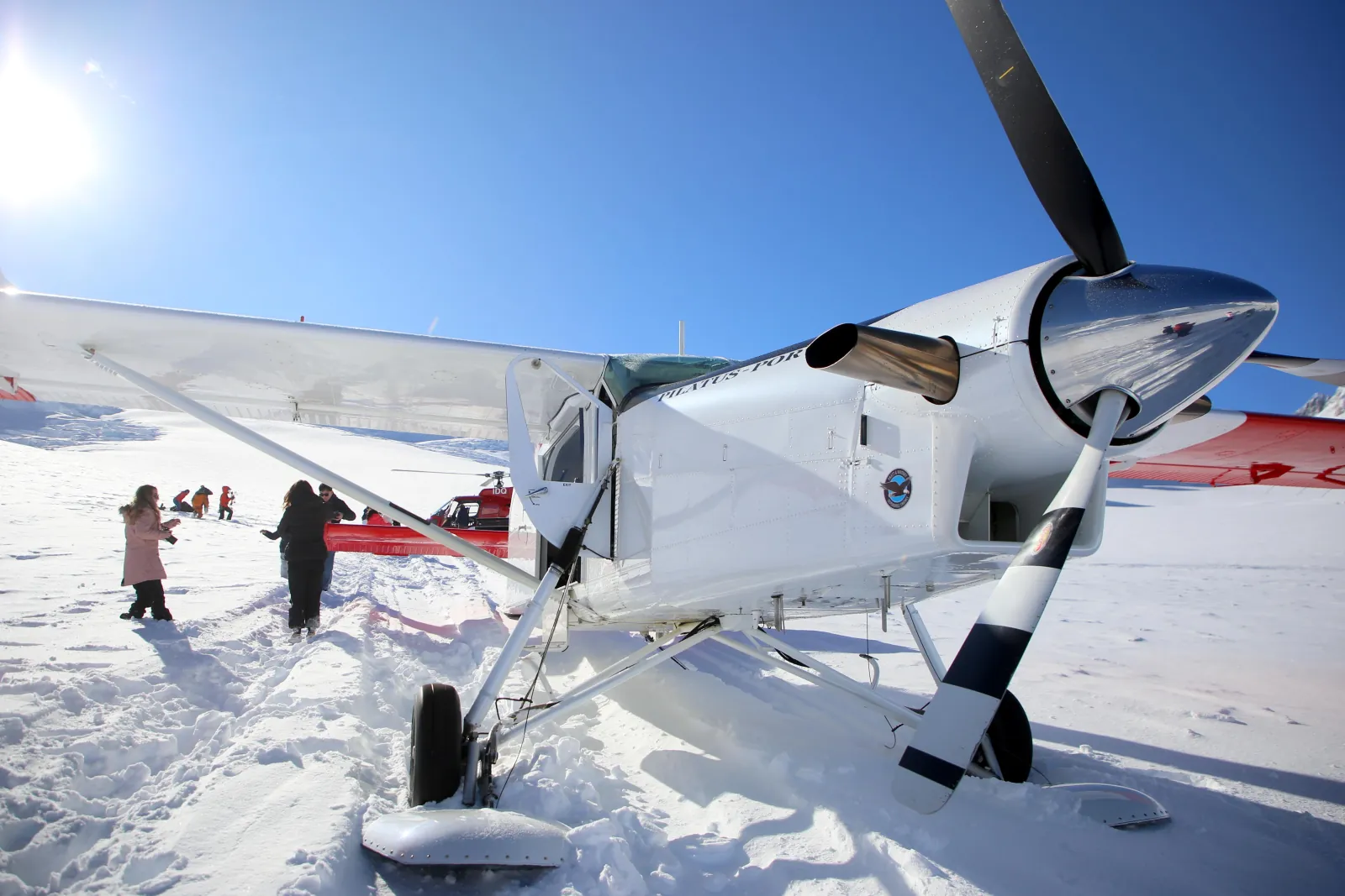 Ski plane propeller and skis on the glacier snow as passengers explore behind it