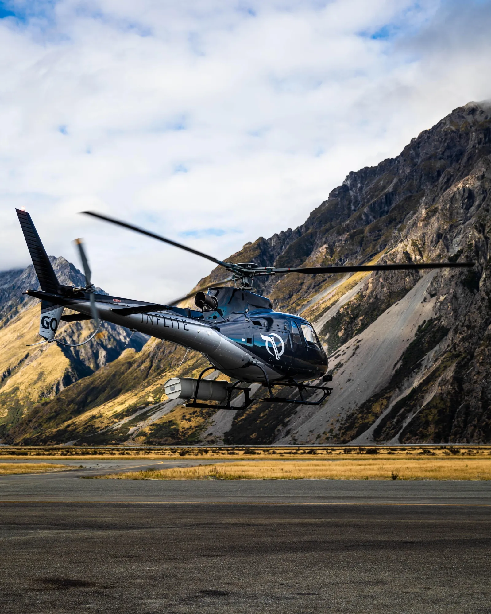 INFLITE helicopter lifting off below a tussock-covered mountainside