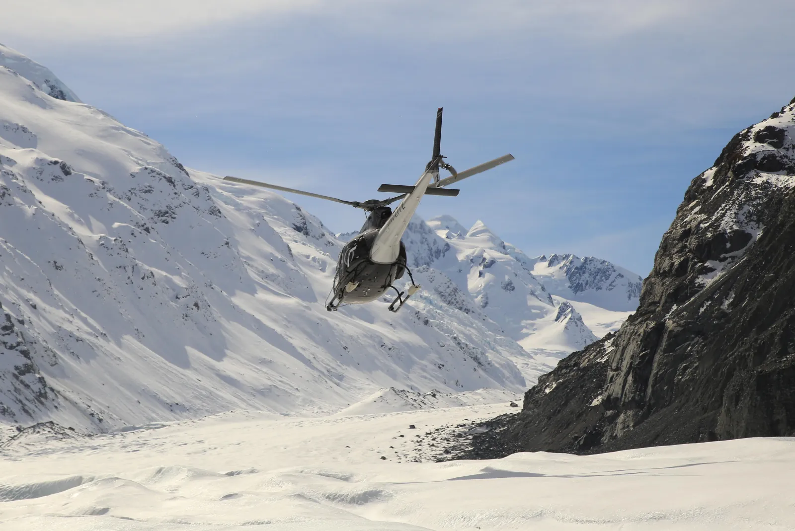 Helicopter flying up a snowy glacier valley between rocky mountain walls