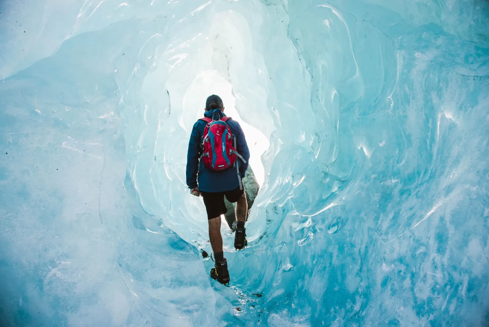 Hiker walking through a turquoise ice tunnel on a guided glacier hike
