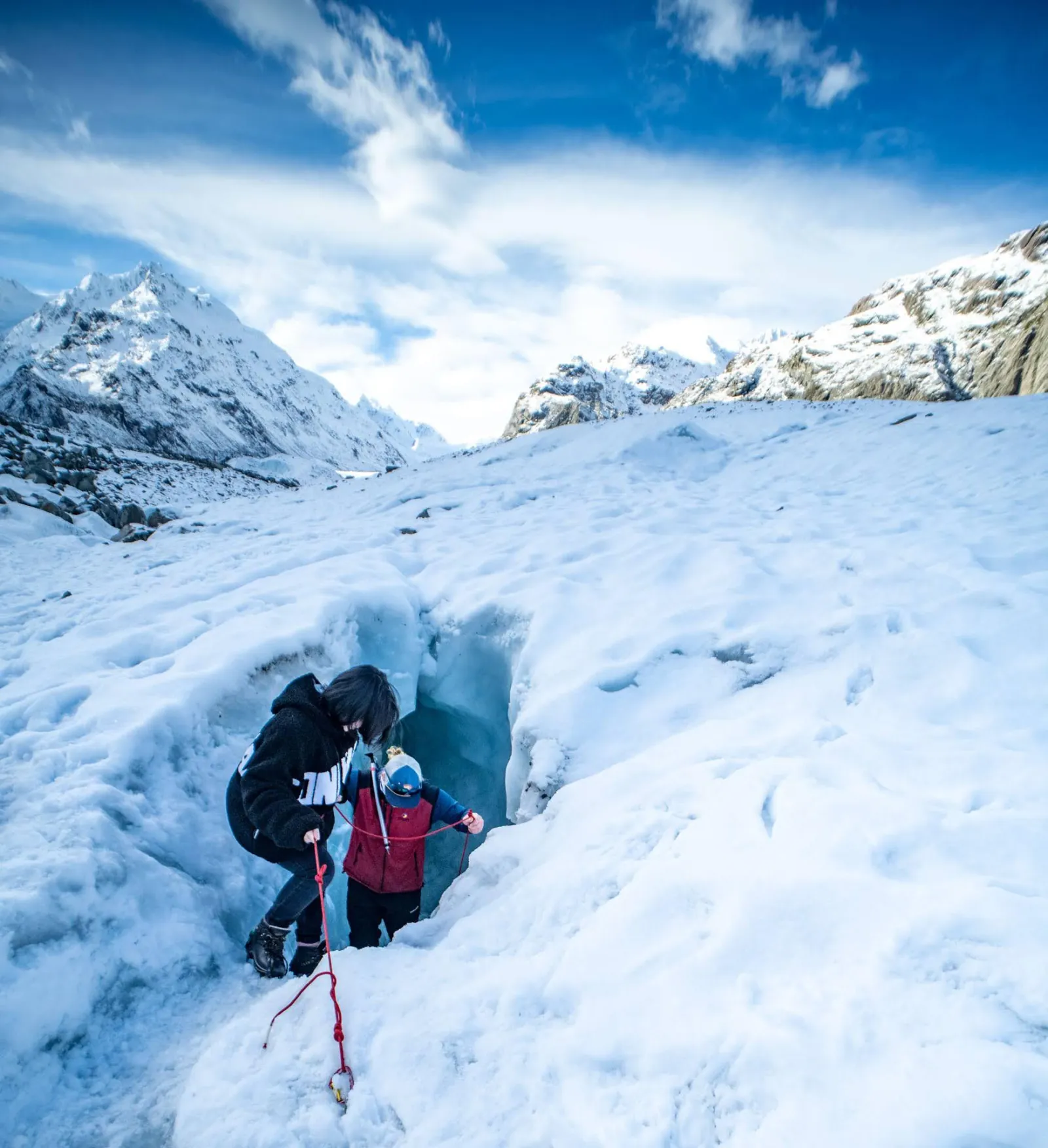 Guide helping a hiker climb out of a snow hollow on the glacier