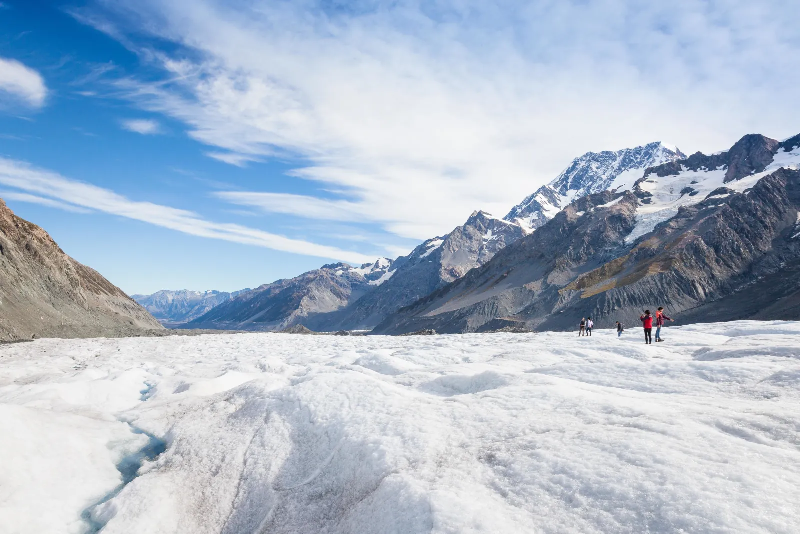 Small group of hikers dwarfed by the wide ice of the Tasman Glacier