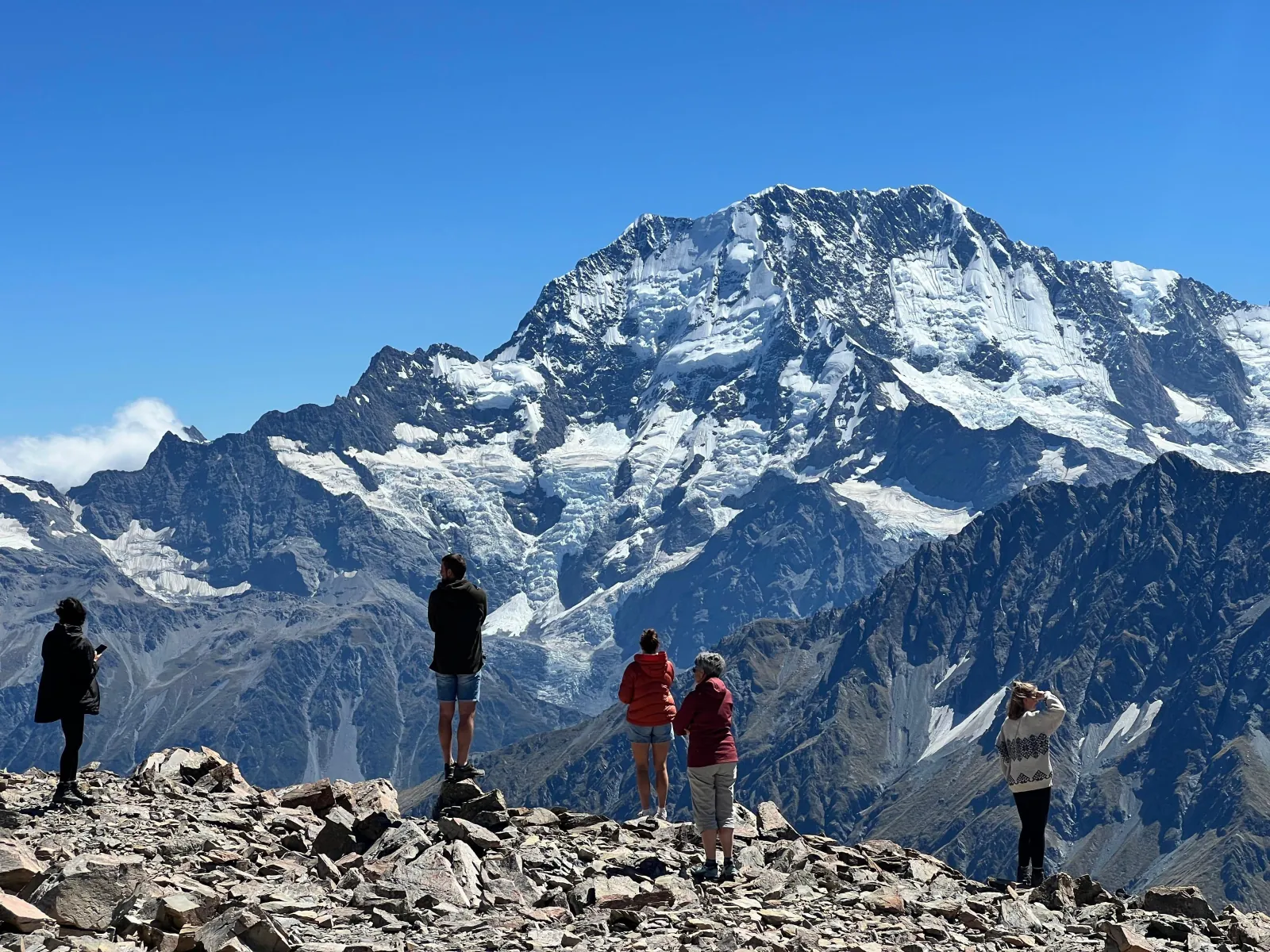 Passengers on a rocky ridge looking at a snow-covered peak in Aoraki/Mount Cook National Park