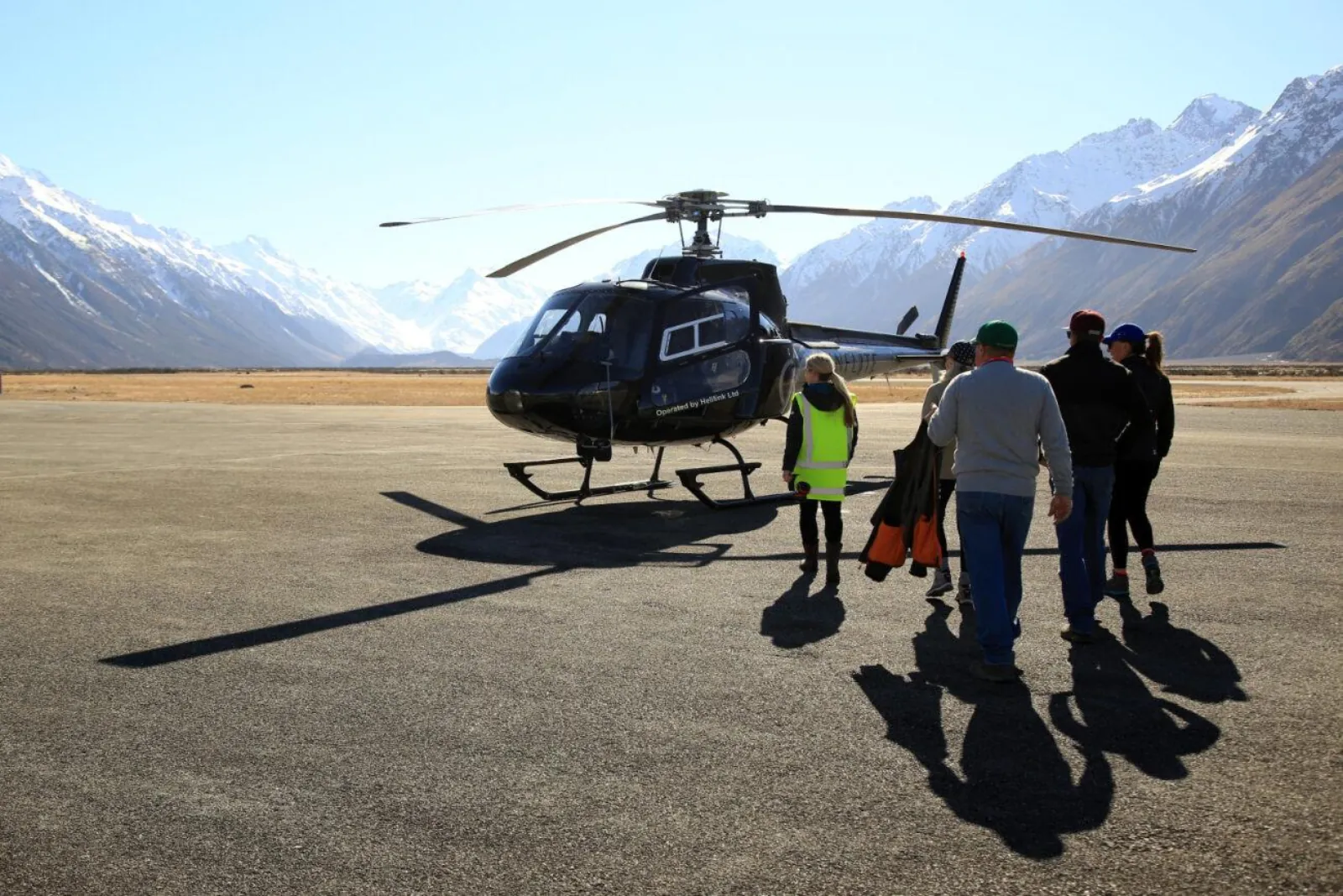 Passengers walking out to a helicopter on the airfield apron with snowy mountains behind