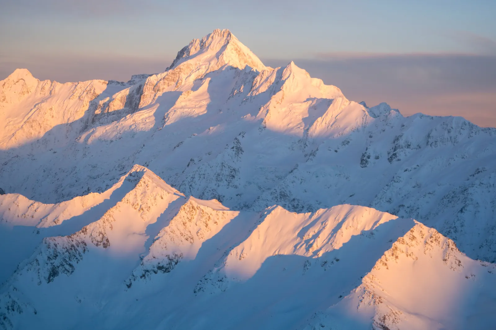 Snow-covered Southern Alps peaks lit pink at sunrise, seen from the air