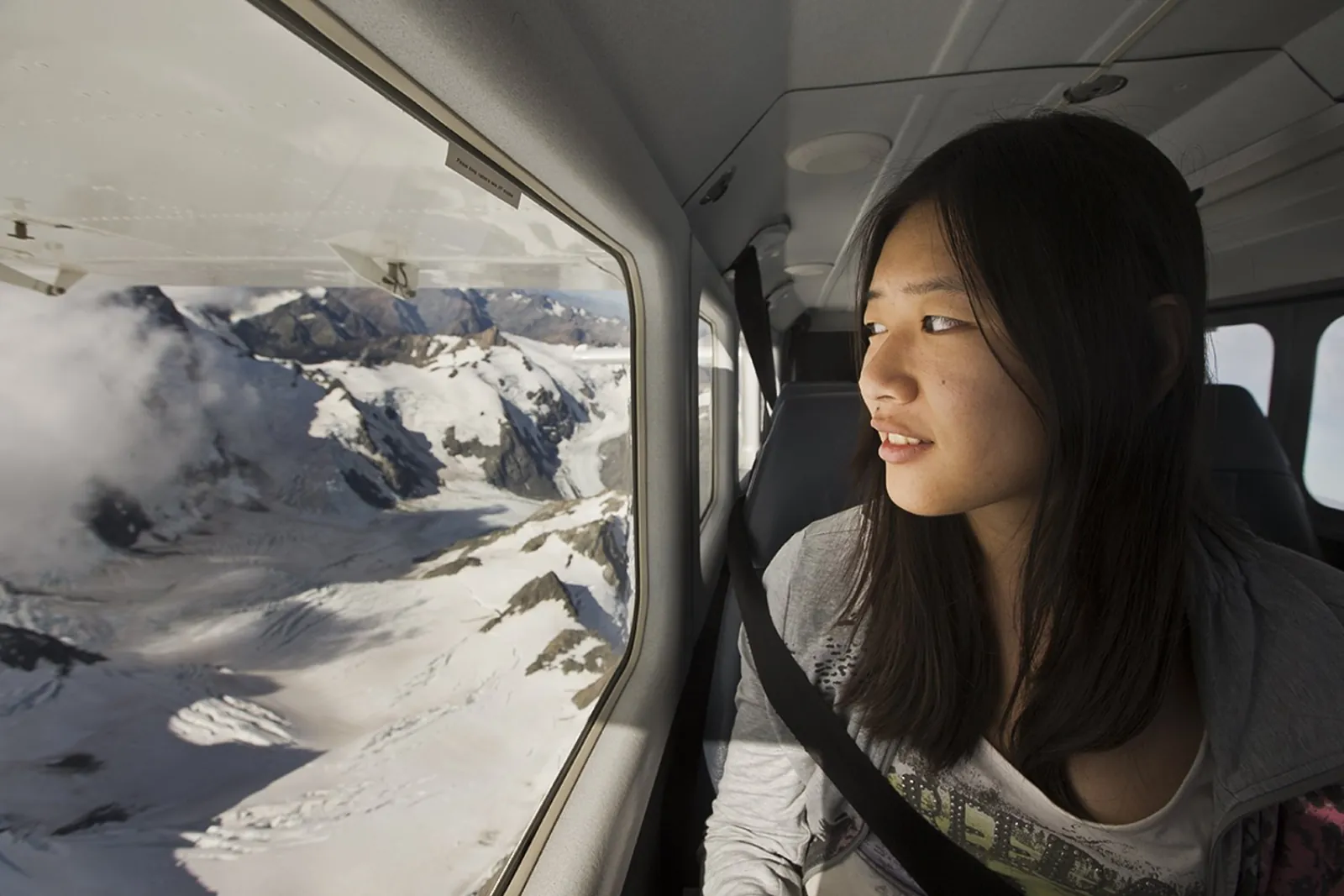 Passenger gazing out of the plane window at glaciers below
