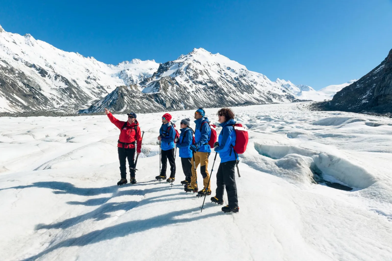 Glacier guide in red leading hikers in blue jackets across the Tasman Glacier