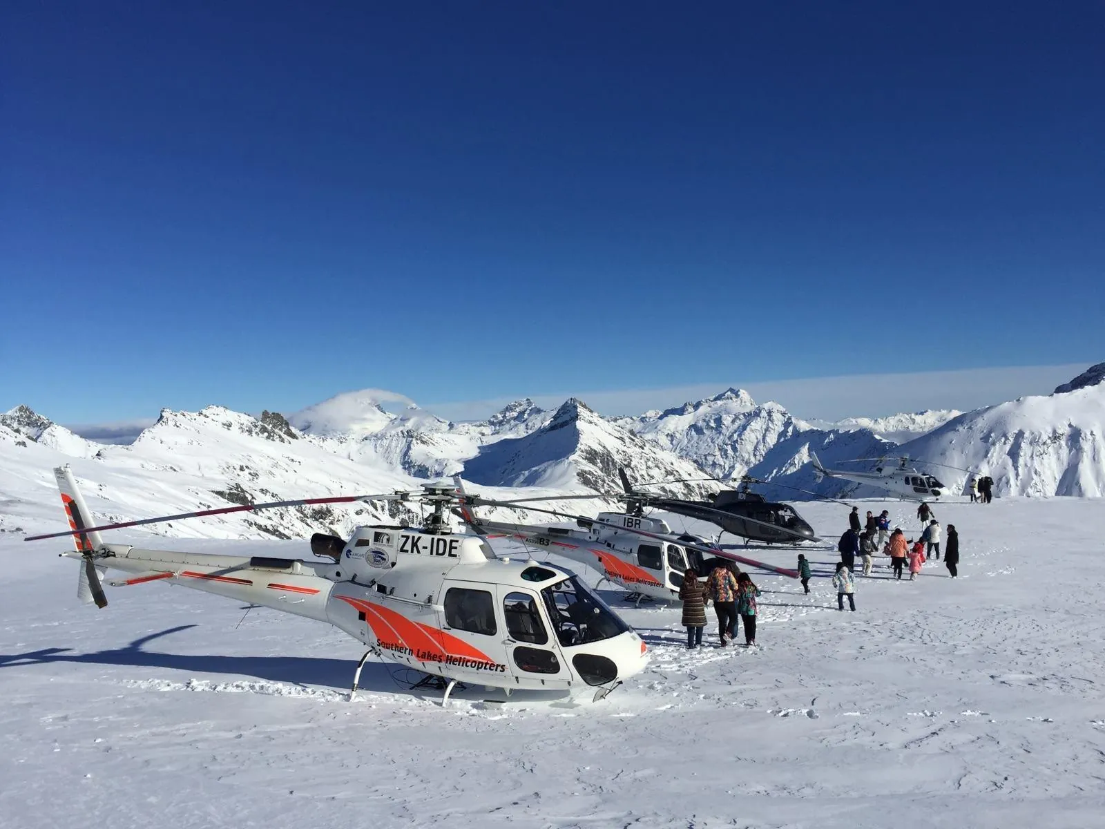 Helicopters parked on a glacier snowfield with passengers walking on the snow