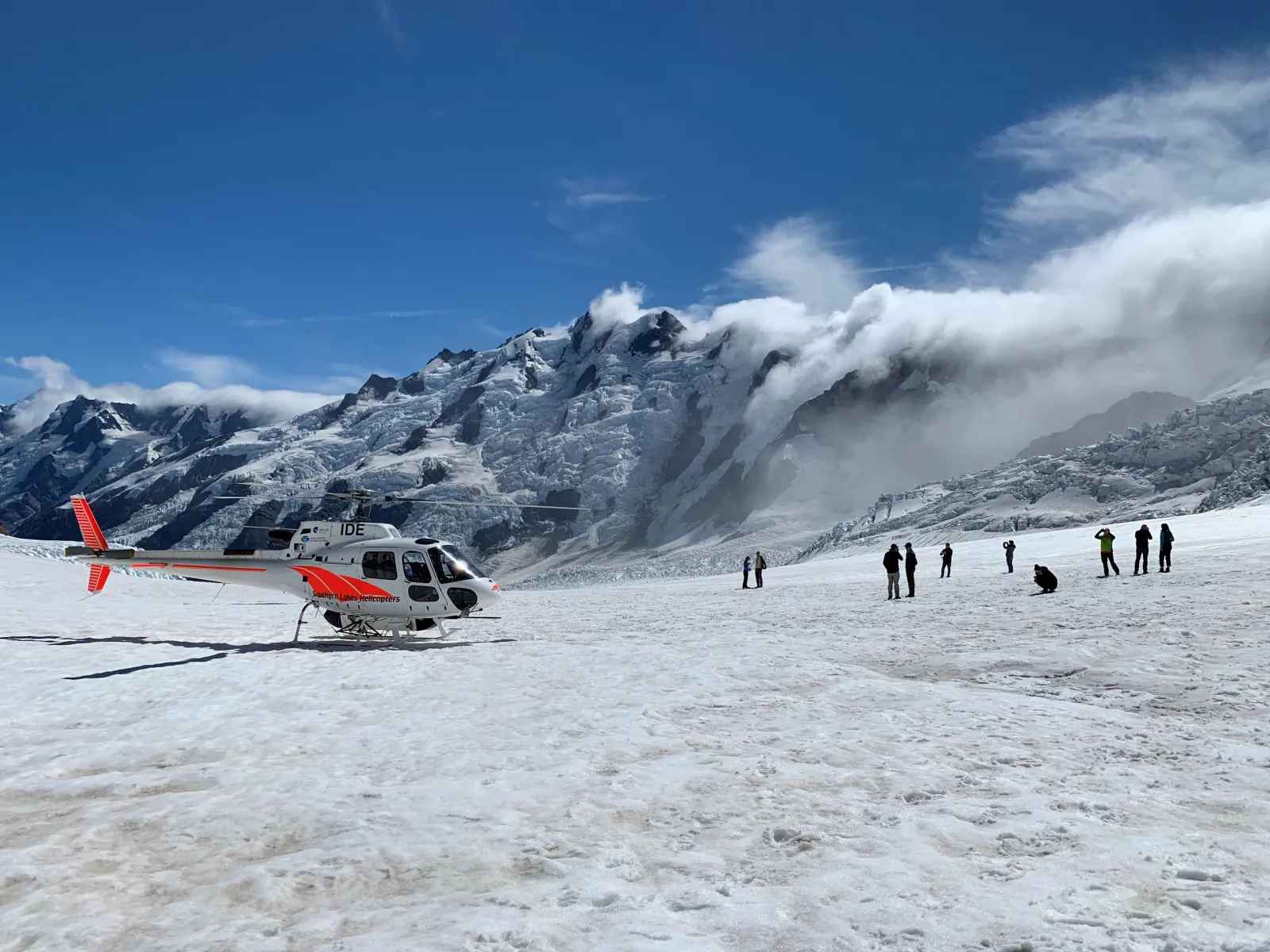 Helicopter on the Tasman Glacier with passengers exploring the snow below cloud-wrapped peaks