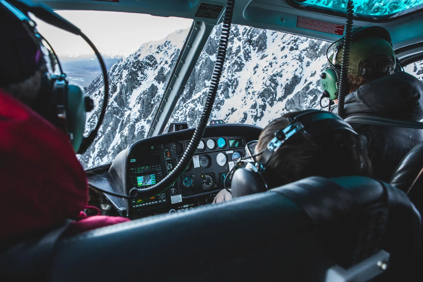 Passengers in headsets looking out of a helicopter cabin at snow-covered rock faces