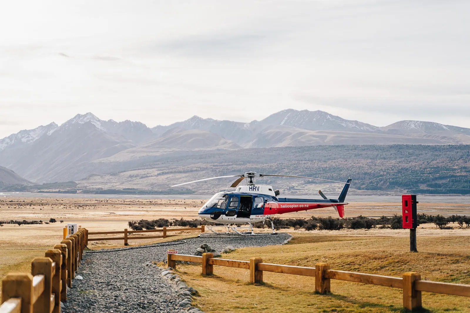 Helicopter on the pad at Glentanner Park, with fenced gravel paths and high-country mountains behind