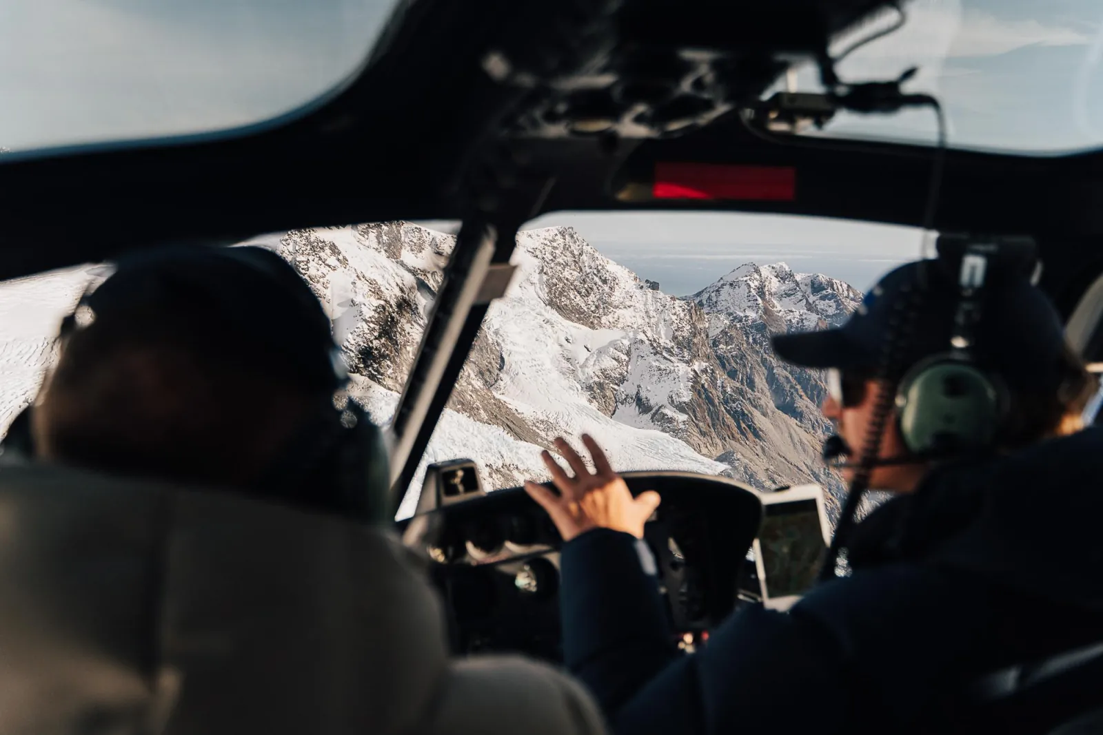 Pilot pointing out snowy peaks through the helicopter windscreen