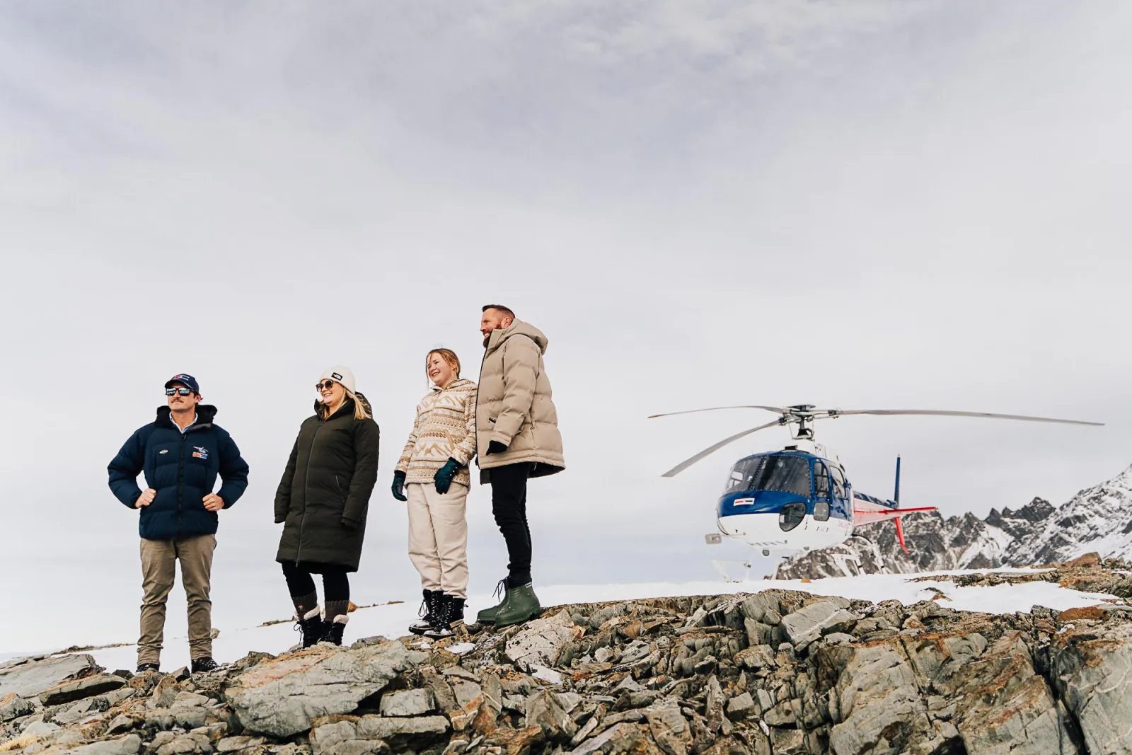 Pilot and three passengers on a rocky alpine landing site beside the helicopter