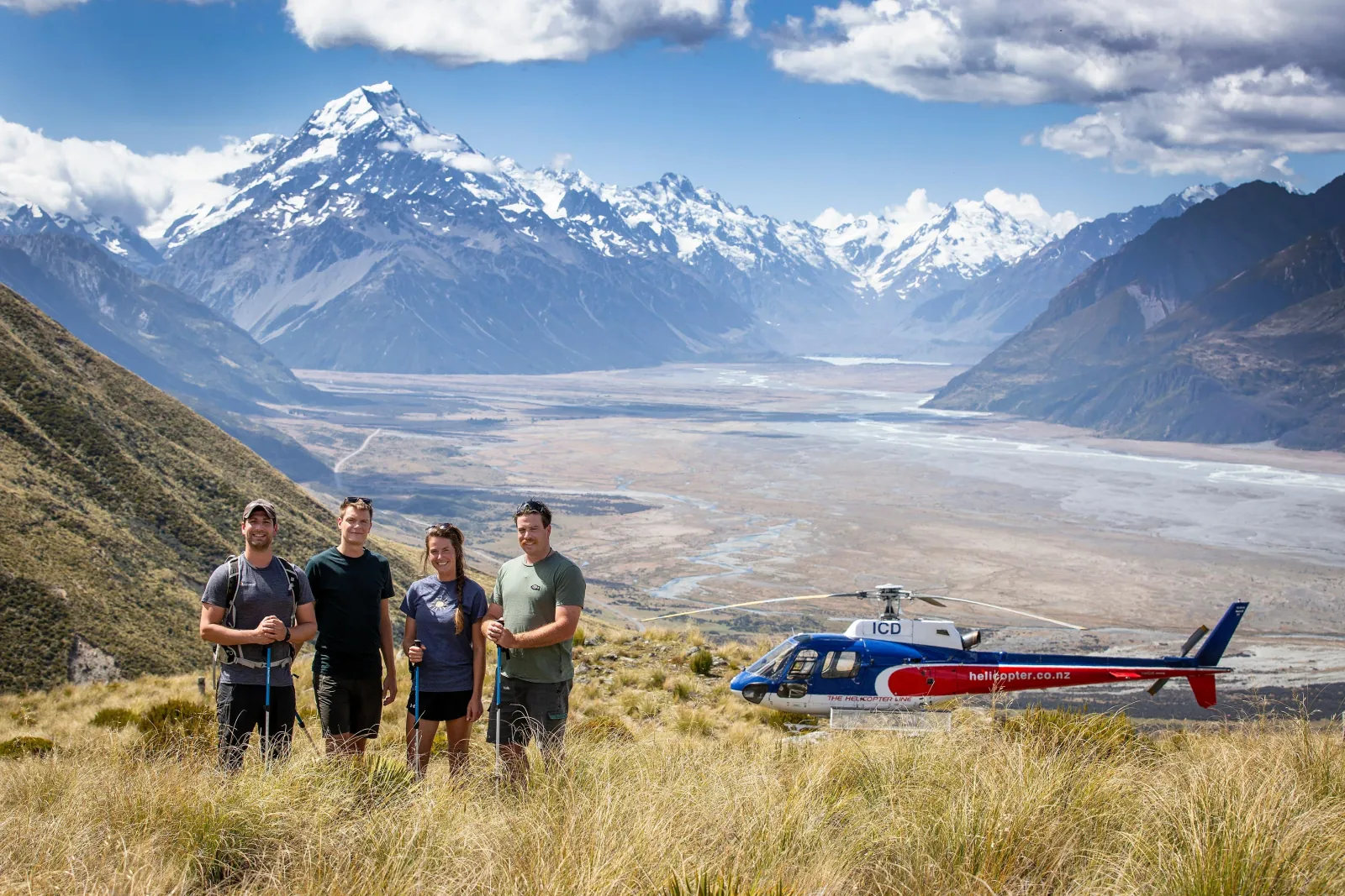 Four hikers beside the helicopter on Glentanner Station's tussock tops, with Aoraki/Mount Cook behind