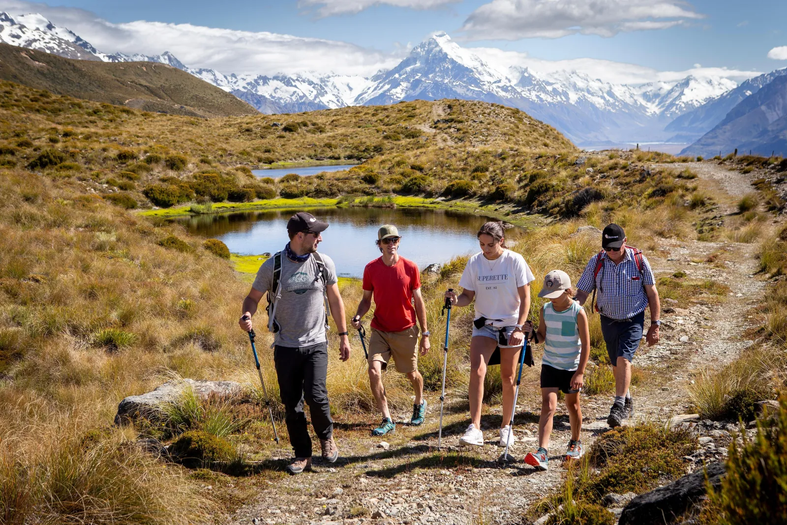 Guide and hikers walking a track past alpine tarns with Aoraki/Mount Cook behind