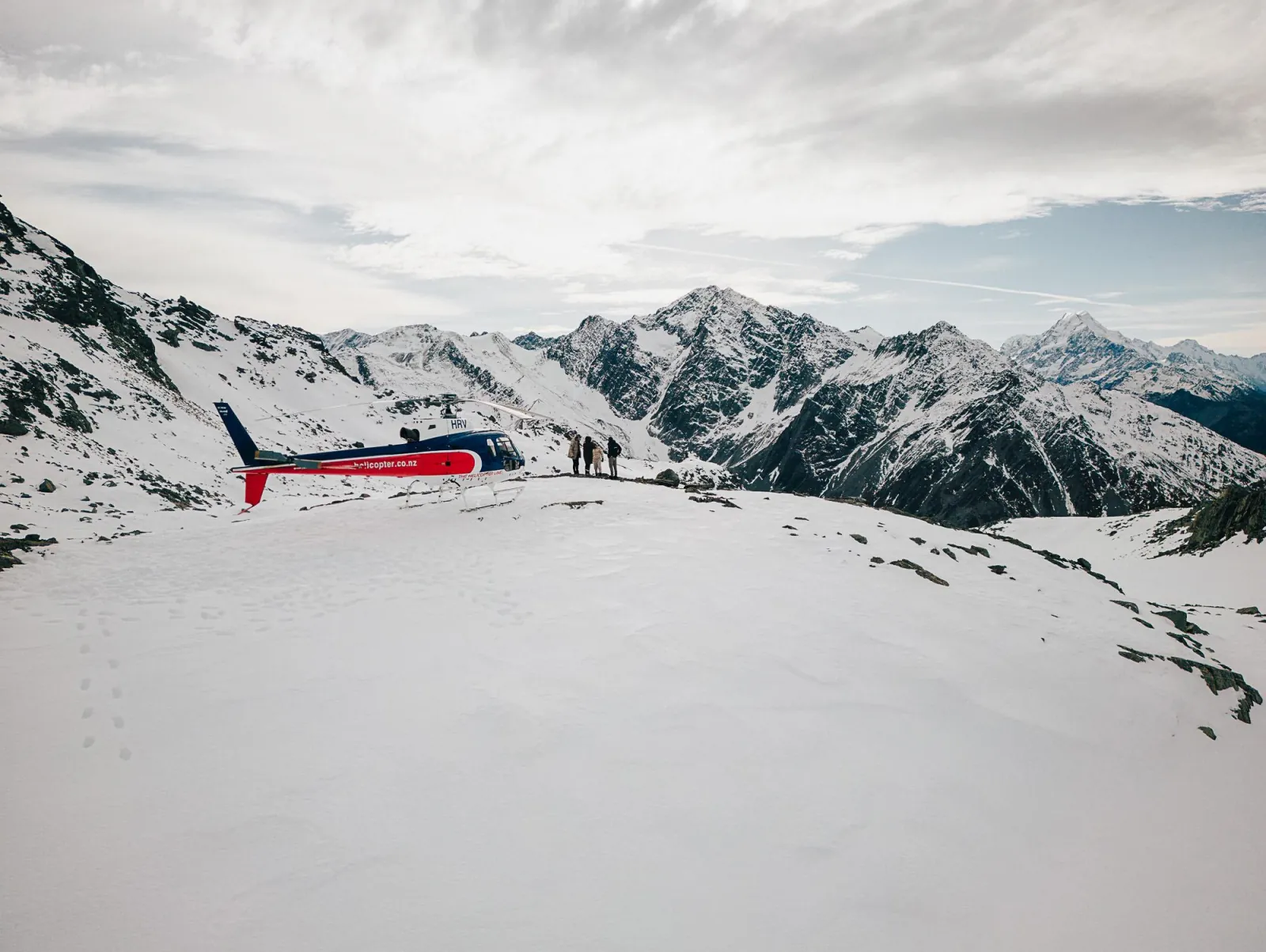 Helicopter and passengers on a wide snowy ridge high in the mountains