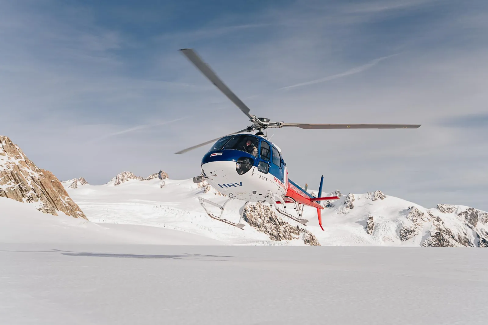 Helicopter hovering above a snowfield with rocky peaks behind