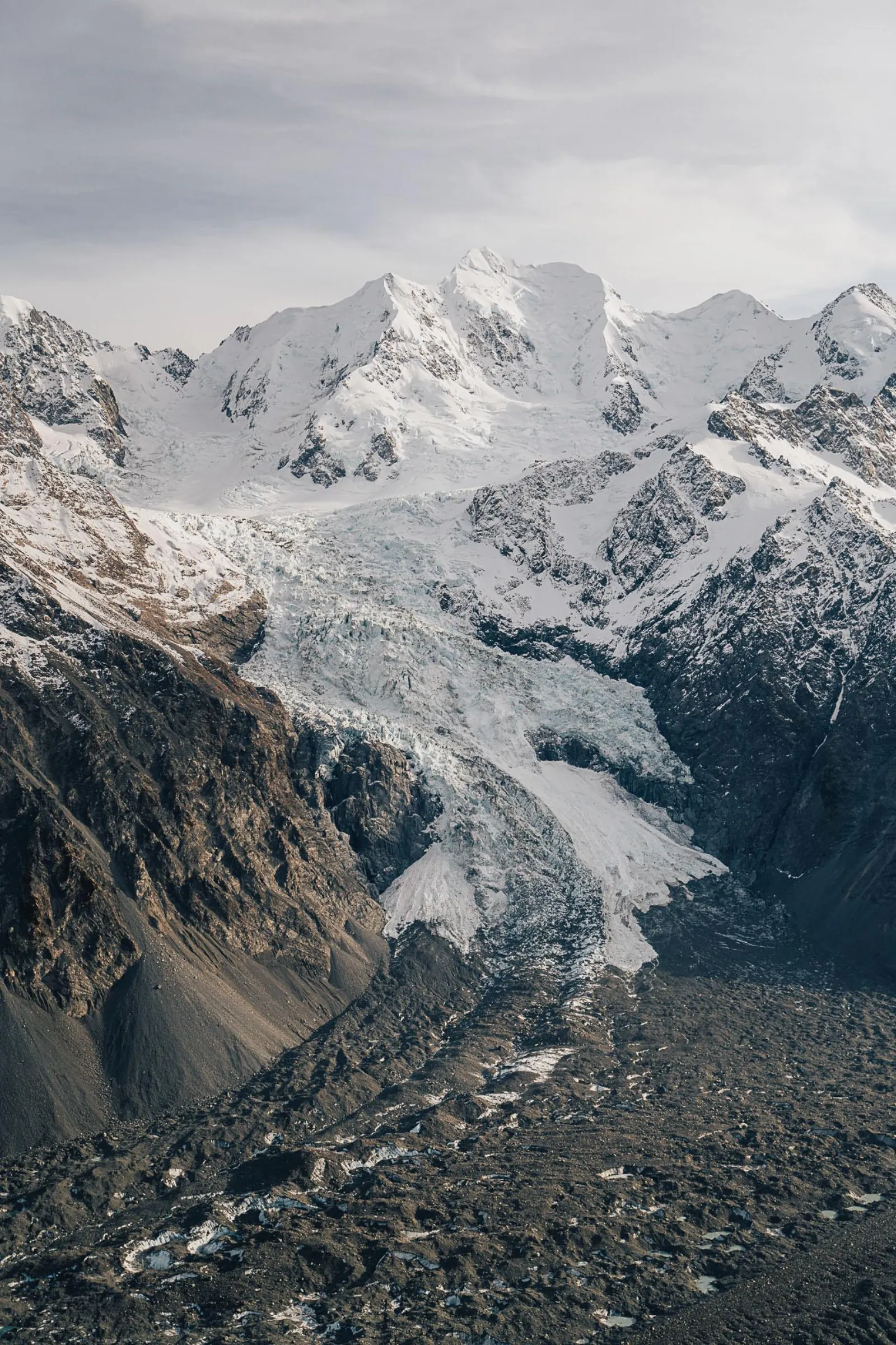 Icefall tumbling down a mountain face above a rubble-covered glacier