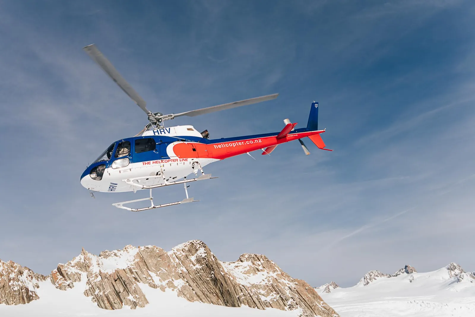 The Helicopter Line helicopter flying above rocky, snow-covered ridges