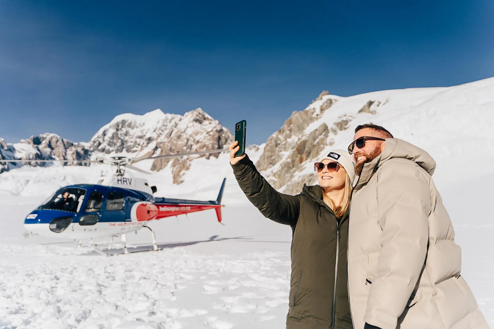 Couple taking a selfie in the snow beside the parked helicopter