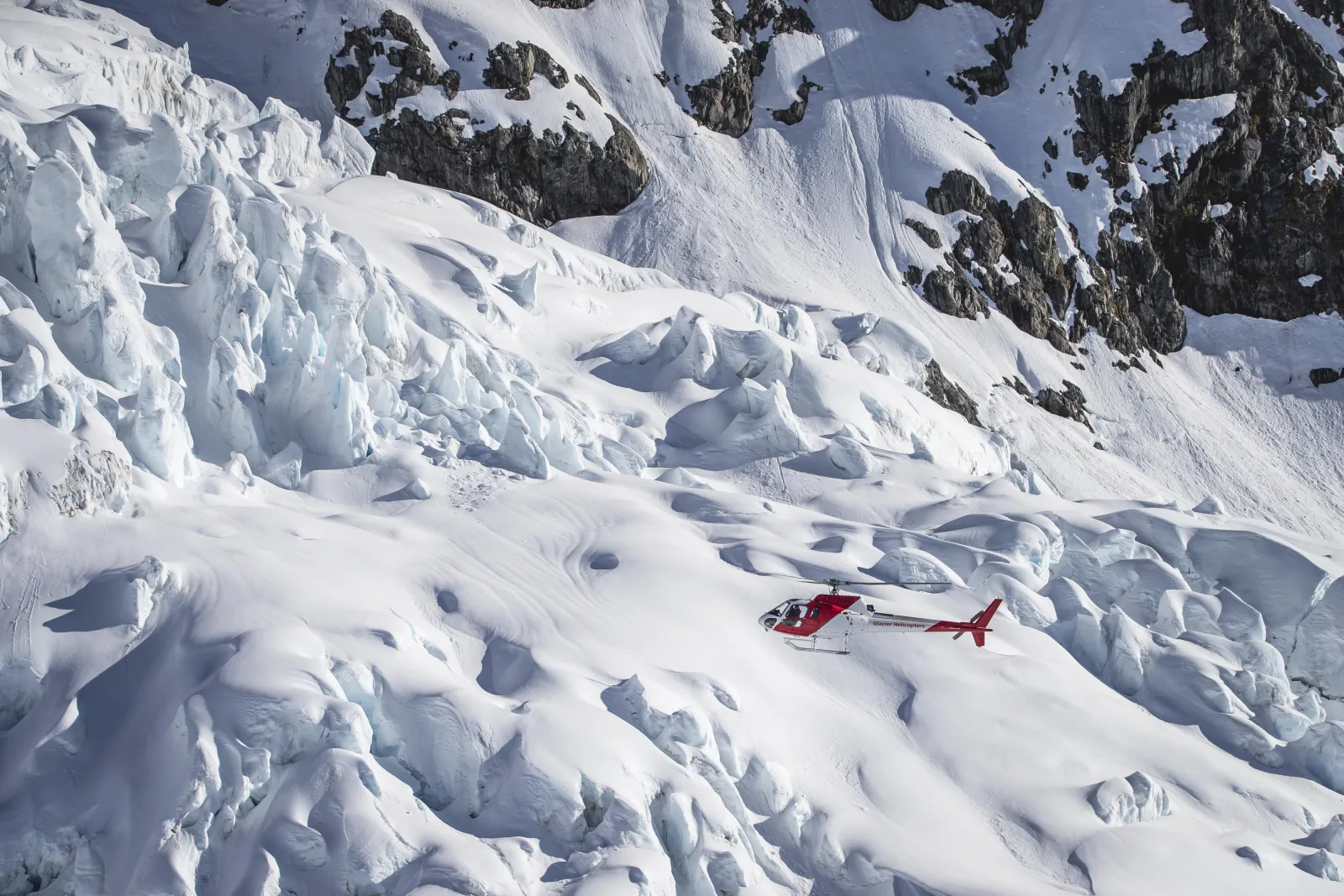 Red and white helicopter hovering above crevassed glacier ice