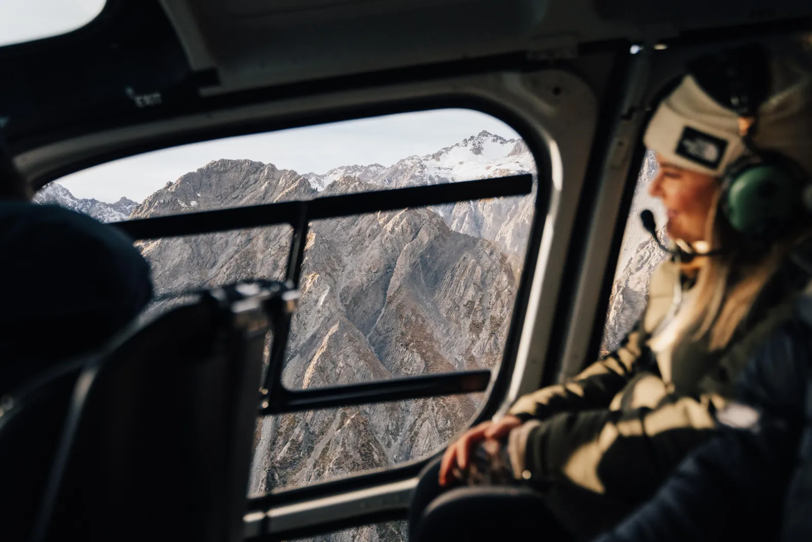 Passenger in a headset looking out of the helicopter window at rocky mountains
