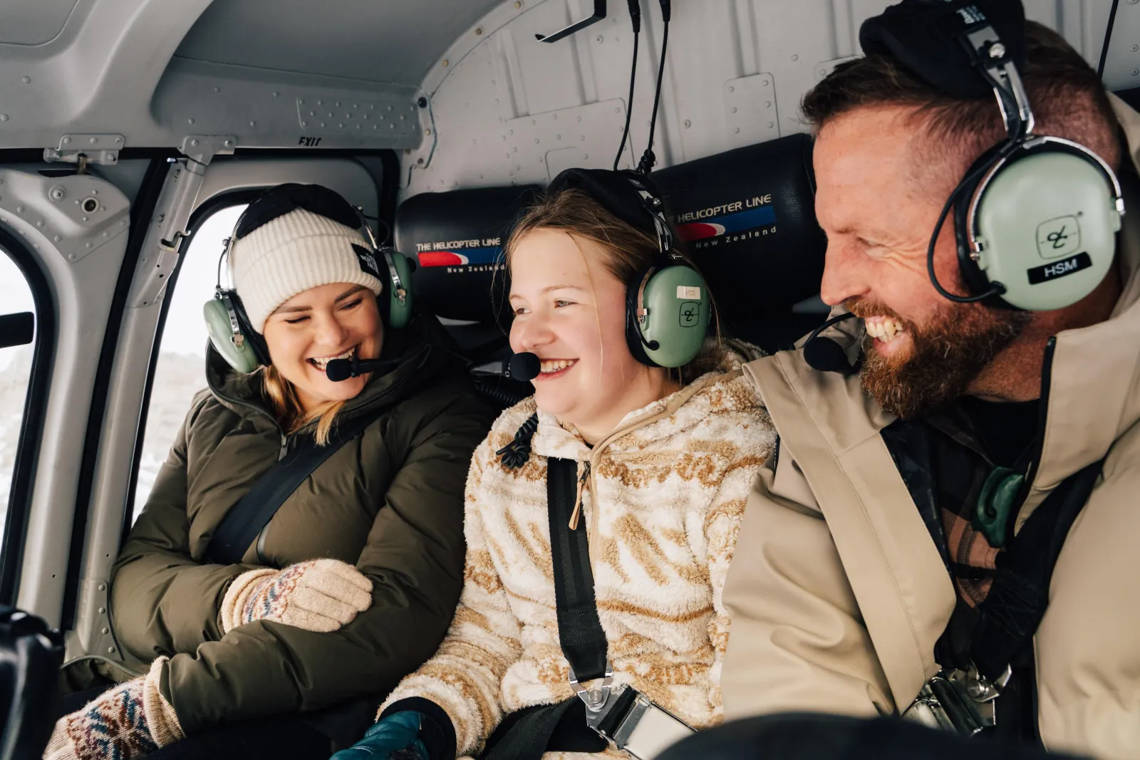 Three passengers in headsets laughing in the back of the helicopter
